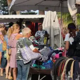Jour de marché à Albenga : des gens flânent devant des étals de vêtements et d'accessoires, sous les palmiers.