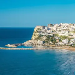 Vue panoramique de Peschici, Italie, avec ses maisons blanches perchées sur la falaise, sa plage de sable fin et son port pittoresque.