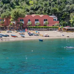 Plage de Vico Equense avec des bateaux colorés sur le sable et dans l'eau turquoise. Bâtiment rose en arrière-plan.