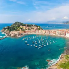 Vue aérienne de la baie de Sestri Levante, avec ses maisons colorées, sa plage et une multitude de bateaux dans les eaux turquoise.