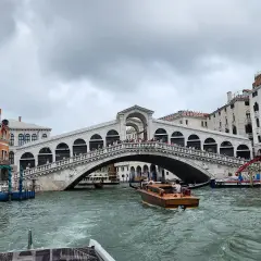 Un taxi venise navigue sur le Grand Canal, passant sous le célèbre pont du Rialto, bordé de bâtiments colorés.