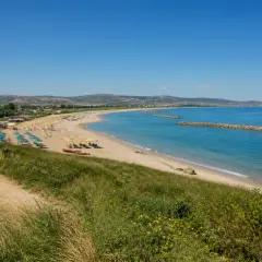 Plage de Pescara, Italie. Parasols bleus et jaunes, mer turquoise, digues en pierre, collines verdoyantes.