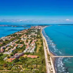 Vue aérienne du Lido di Venezia, une longue bande de terre bordée par la mer Adriatique et la lagune, avec des maisons, des arbres et des digues.