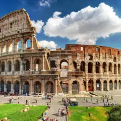 Le Colisée de Rome en août, baigné de soleil, accueille des visiteurs sous un ciel bleu parsemé de nuages.