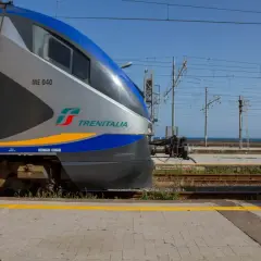 Le train Trenitalia ME 040, prêt à partir pour un voyage en train en Sicile, attend sur les rails sous un ciel bleu clair.