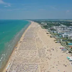Plage bondée de parasols et de baigneurs à Bibione, Italie, avec la mer turquoise et des hôtels en arrière-plan.