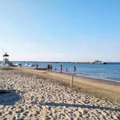 Plage animée à Gatteo Mare, avec des baigneurs, des enfants jouant dans l'eau et un poste de secours. Un bateau navigue au loin.
