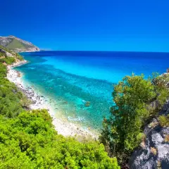 Vue panoramique de la côte de **Sardaigne Cala Gonone**, avec ses eaux turquoise cristallines, sa plage de galets et sa végétation luxuriante.