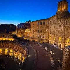 Les marchés de Trajan s'illuminent dans la nuit romaine, vestiges antiques baignés d'une douce lumière dorée sous un ciel bleu profond.