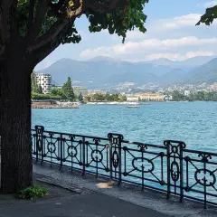 Vue paisible du lac de Lugano, avec une promenade bordée d'arbres et de montagnes en arrière-plan.