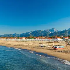 Plage de sable fin à Forte dei Marmi, Italie, avec des rangées de parasols blancs et des montagnes majestueuses en arrière-plan.