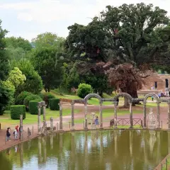Vestiges antiques et étang reflétant le ciel à la Villa Adriana de Tivoli. Des colonnes romaines bordent l'eau, entourées de verdure luxuriante.