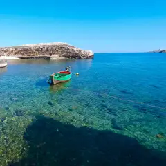 Un bateau vert et rouge flotte dans les eaux cristallines de Polignano a Mare, dans les Pouilles. Le soleil brille sur la mer Adriatique.