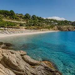 Plage de galets et eaux turquoises à Alassio, Italie. Des rangées de parasols et de chaises longues invitent à la détente sous le soleil.