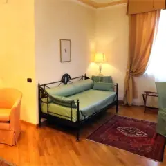 Chambre confortable dans un des hôtels de Castiglione Tinella, avec un lit de repos vert, un fauteuil orange et des rideaux dorés.