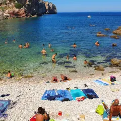 Plage de galets à Terrasini, Sicile. Des baigneurs profitent de l'eau cristalline sous un soleil radieux.