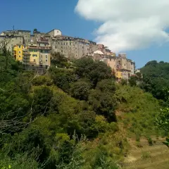Village d'Ameglia perché sur une colline verdoyante, avec des maisons colorées et un ciel bleu éclatant.