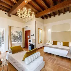 Suite luxueuse au **hotel Cariola Caprino Veronese** avec lit king-size, canapé, lustre et vue sur jardin tropical.