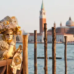 Une personne masquée et costumée, prête pour le carnaval, pose près de l'eau. Une belle image pour savoir quand aller à Venise.