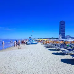 Plage animée à Cesenatico, Italie, avec des parasols rayés, des chaises longues et des baigneurs profitant du soleil sous un ciel bleu éclatant.
