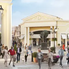 Des promeneurs profitent d'une journée ensoleillée au Castel Romano Outlet, admirant les vitrines et l'art.