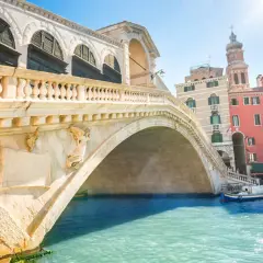 Le célèbre pont du Rialto à Venise, avec ses arches majestueuses et ses bâtiments colorés en arrière-plan, se reflète dans les eaux turquoise du Grand Canal.