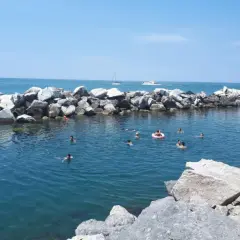 Baignade estivale dans la marina de Pise, avec des rochers formant une digue et des baigneurs profitant du soleil.