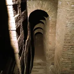 Passage voûté dans les catacombes de Rome, avec des niches creusées dans le mur de briques.