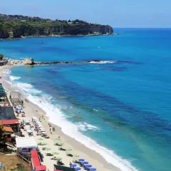 Plage animée à Tropea, Italie, avec des parasols colorés, des baigneurs et des falaises verdoyantes surplombant la mer d'un bleu éclatant.