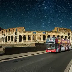 Un bus de nuit Rome passe devant le Colisée sous un ciel étoilé.