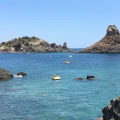 Vue sur la mer bleue et les rochers volcaniques d'Aci Trezza, Sicile. Des bateaux et des baigneurs profitent du soleil.