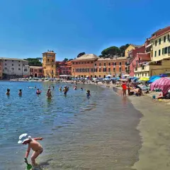 Plage animée à Chiavari, Italie, avec des baigneurs dans l'eau et des parasols colorés sur le sable.