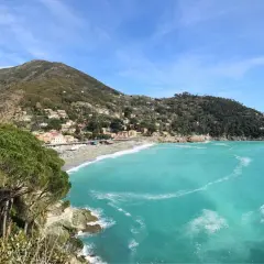 Vue panoramique de la baie de Bonassola en Italie, avec ses eaux turquoise, sa plage animée et ses collines verdoyantes couvertes de maisons.