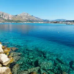 Vue sur la mer turquoise et les montagnes de Capo San Vito. Des rochers blancs bordent la côte.