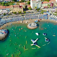 Plage animée à Arma di Taggia, Italie, avec des parasols bleus et blancs, des baigneurs dans la mer turquoise et des structures gonflables.