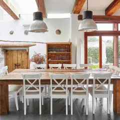 Salle à manger rustique d'un agriturismo en Ligurie, avec table en bois massif, chaises blanches et grande porte vitrée donnant sur le jardin.