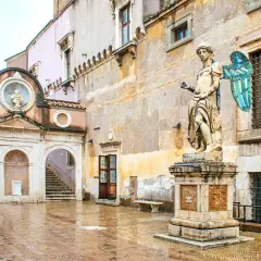 Intérieur du **château Saint-Ange** : une cour pavée et humide, une statue d'ange imposante, une arche menant à un escalier et des fenêtres grillagées.