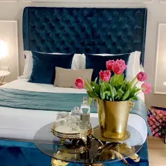 Chambre d'hôte en Lombardie : lit luxueux avec tête de lit capitonnée bleue, tulipes roses et tables de chevet élégantes.