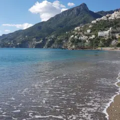 La plage de Vietri sul Mare s'étend sous un ciel bleu, avec des maisons blanches perchées sur la colline verdoyante. L'eau turquoise caresse le sable.