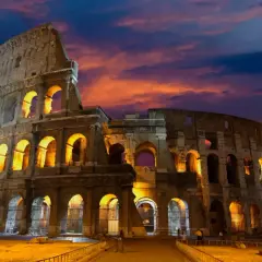 Le Colisée de nuit, illuminé par des lumières chaudes, se dresse sous un ciel aux couleurs flamboyantes.