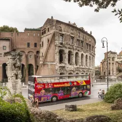 Un bus touristique rouge vif, "Citysightseeing Roma", passe devant des ruines antiques et des bâtiments romains.