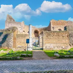 Ruines antiques sur l'Appia Antica à Rome, sous un ciel bleu parsemé de nuages blancs.