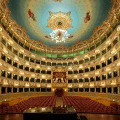 L'intérieur doré et orné du théâtre La Fenice, avec ses loges superposées, ses lustres étincelants et son plafond peint, prêt à accueillir un concert.