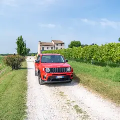 Une voiture rouge Jeep sur un chemin de gravier en Italie, près d'un vignoble. Le prix de cette voiture est très attractif.