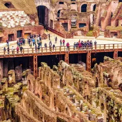 Vue d'ensemble de l'arène du Colisée à Rome, avec des touristes sur une passerelle surplombant les ruines antiques.