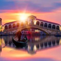Gondole glissant sur le Grand Canal, sous un ciel aux couleurs vibrantes, avec le célèbre pont du Rialto en arrière-plan. Une scène qui évoque une célèbre peinture de Venise.
