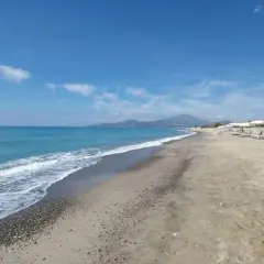 Plage de sable et de galets à Ascea Marina, avec des vagues bleues, des parasols blancs et des montagnes à l'horizon.