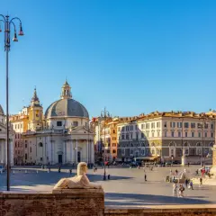 La Piazza del Popolo à Rome, avec ses églises jumelles, son obélisque et son sphinx, sous un ciel bleu éclatant.