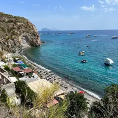 Plage animée à Lipari, avec des parasols, des petits restaurants et des bateaux naviguant sur la mer turquoise.