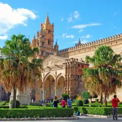 La cathédrale de Palerme, capitale Sicile, se dresse fièrement sous un ciel bleu, entourée de palmiers et de jardins verdoyants.